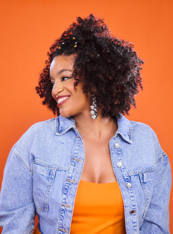 Woman with curly hair smiling, showcasing Mielle Organics products.