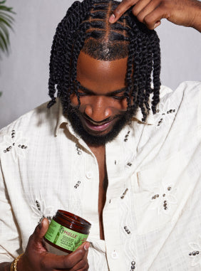 Man with braids holding Mielle Organics hair product, smiling.