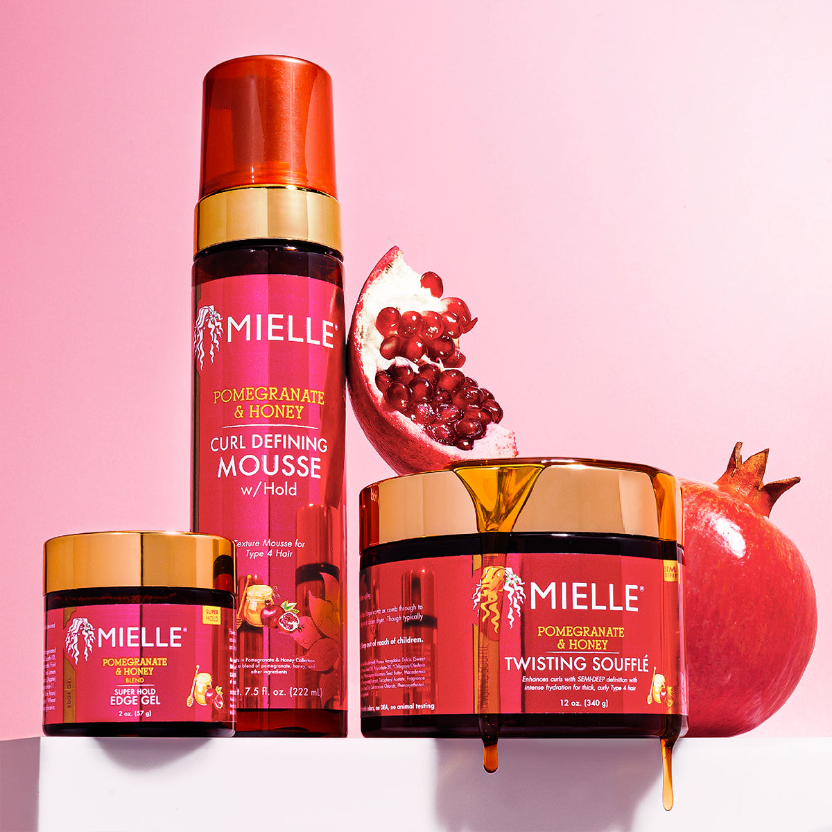 Mielle Pomegranate & Honey hair care products with pomegranate slices on a pink background