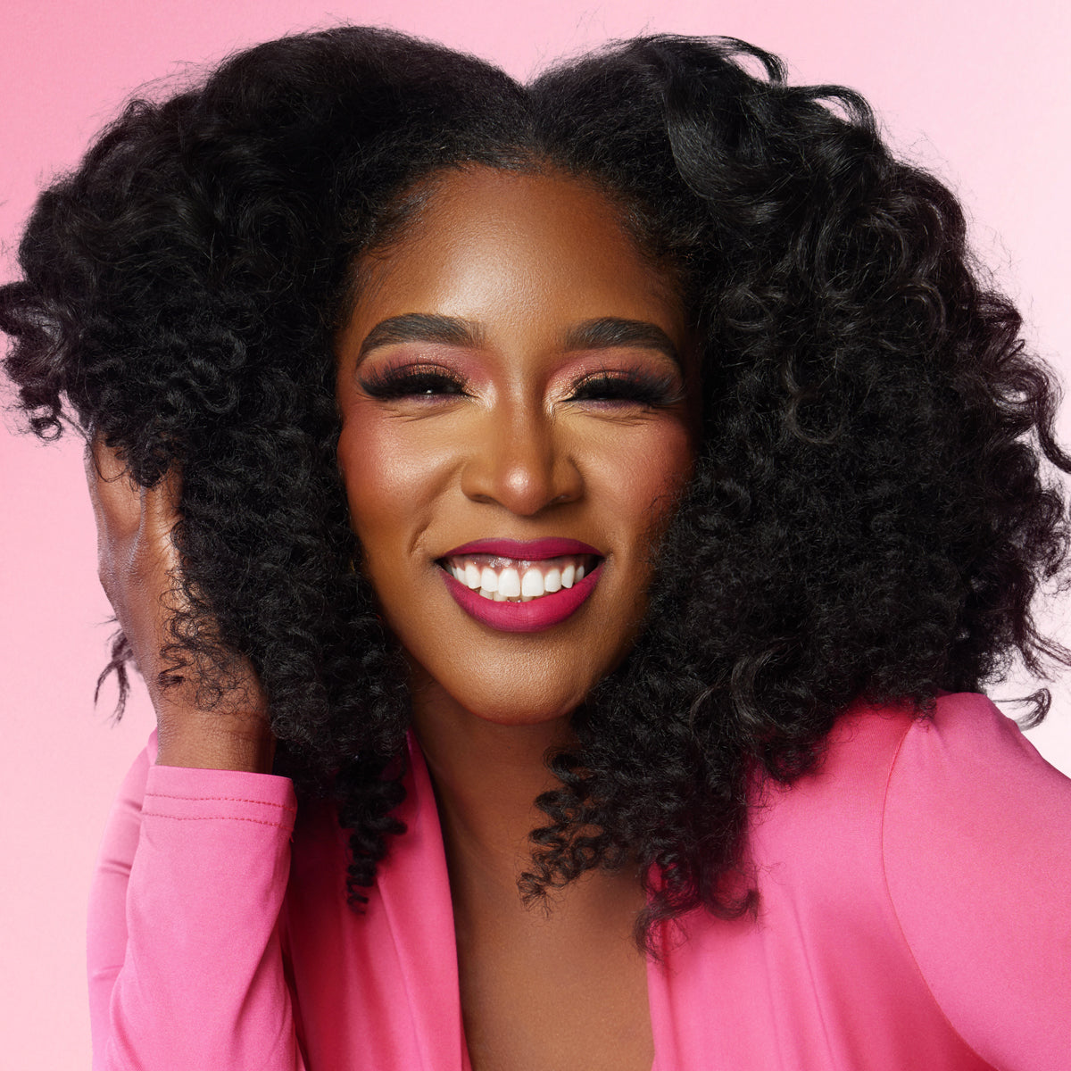 Woman with styled hair wearing a pink outfit against a pink background