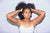 Athletic Afro-american girl in white tank top holding her hair up with both hands, looking confident